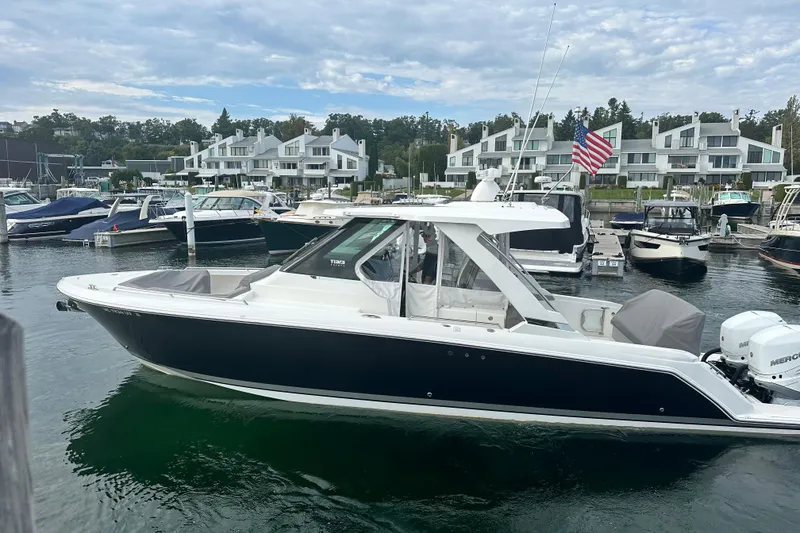 Slide: The Image of 2023 Tiara Yachts 34 LS docked in a marina with modern buildings in the background. - 3