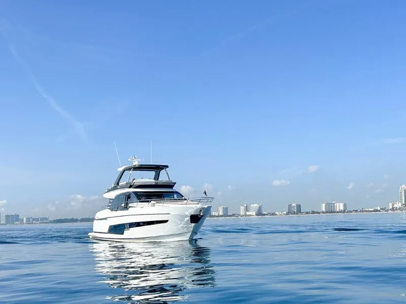 Slide: The Image of 2024 Fairline Squadron 68 yacht cruising on calm waters with city skyline in the background. - 2