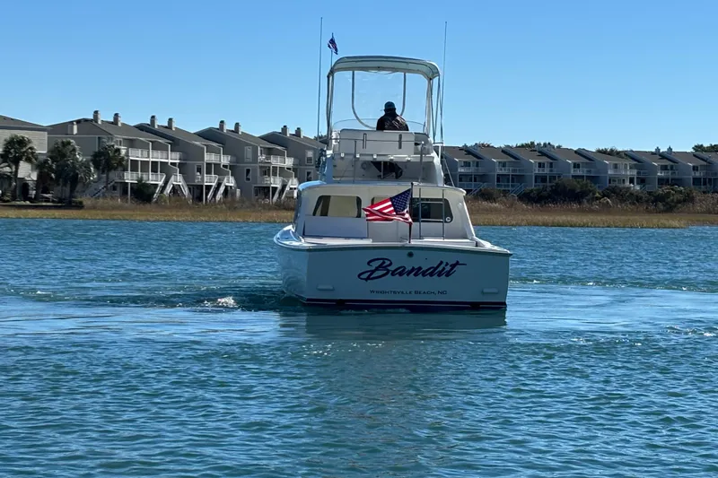 Slide: The Image of 1970 Bertram 31 Flybridge Cruiser on water near coastal homes, displaying American flag. - 10
