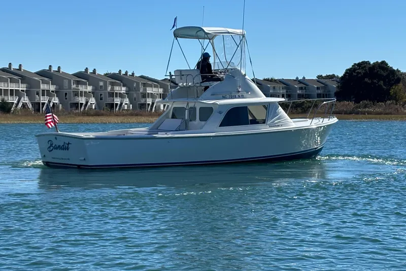 Slide: The Image of 1970 Bertram 31 Flybridge Cruiser on water, with American flag, near waterfront homes. - 13