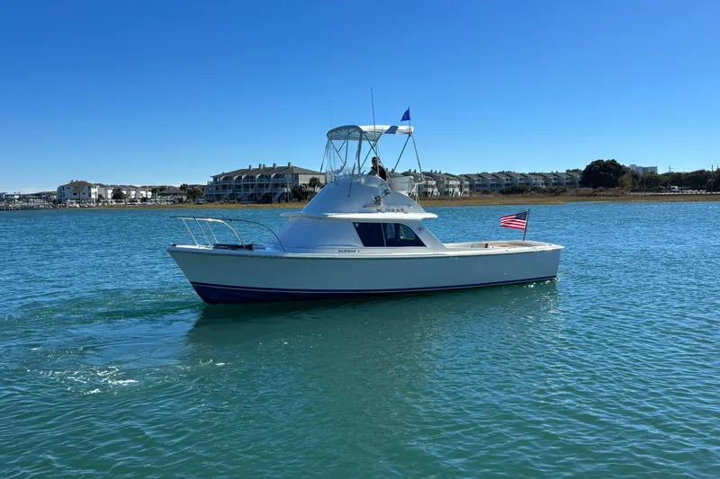 Slide: The Image of 1970 Bertram 31 Flybridge Cruiser on calm water, American flag, clear blue sky. - 17