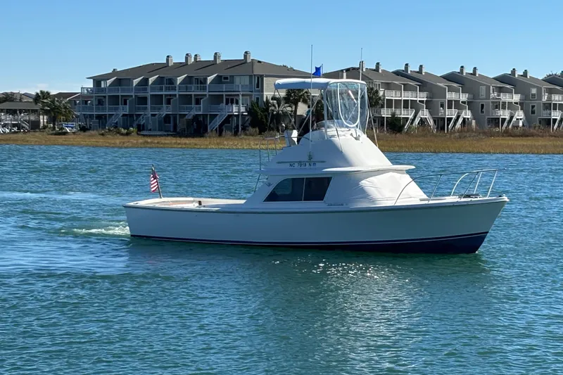 Slide: The Image of 1970 Bertram 31 Flybridge Cruiser on water near waterfront homes, clear sky. - 3