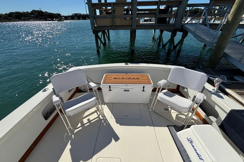 Slide: The Image of 1970 Bertram 31 Flybridge Cruiser deck with chairs and cooler, docked by sparkling water. - 35