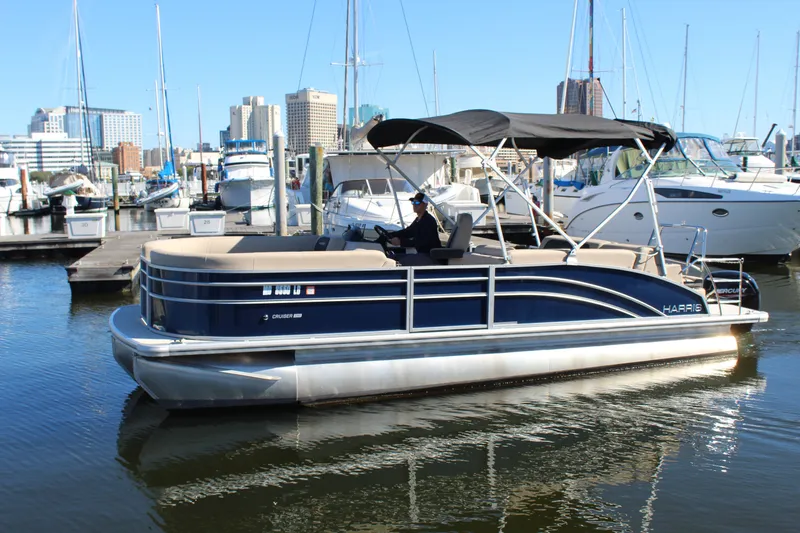 Slide: The Image of 2025 Harris Cruiser 230 pontoon boat docked in a marina with city skyline. - 2