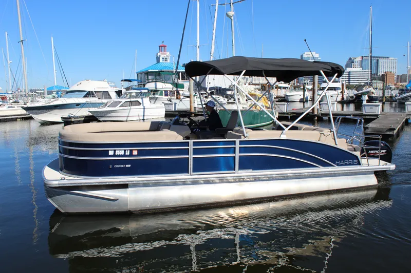 Slide: The Image of 2025 Harris Cruiser 230 pontoon boat docked in a marina under clear blue skies. - 3