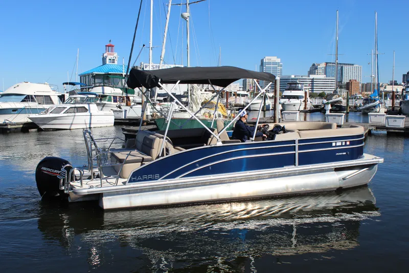 Slide: The Image of 2025 Harris Cruiser 230 pontoon boat docked in a marina with city skyline. - 7