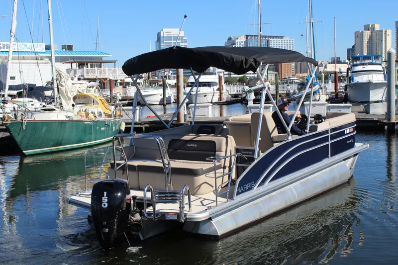 Slide: The Image of 2025 Harris Cruiser 230 pontoon boat docked in a marina with cityscape background. - 8