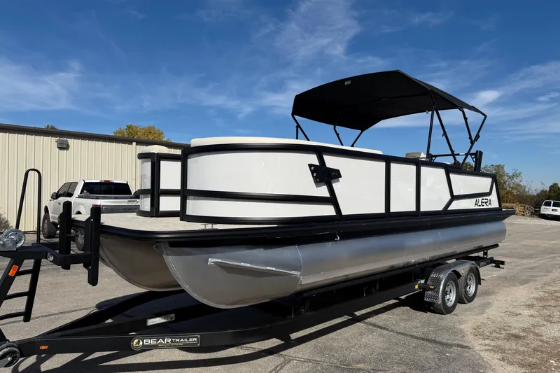 Slide: The Image of 2026 Alera M 25L pontoon boat on trailer, parked outdoors under clear sky. - 3