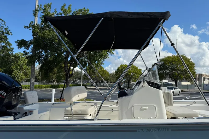 Slide: The Image of 2025 Boston Whaler 170 Montauk boat with canopy, parked outdoors under a clear sky. - 7