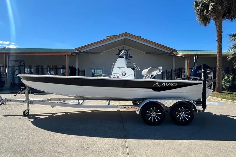 The Image of 2026 Avid 21 FST boat on trailer, parked outside a building under clear blue sky. - 0