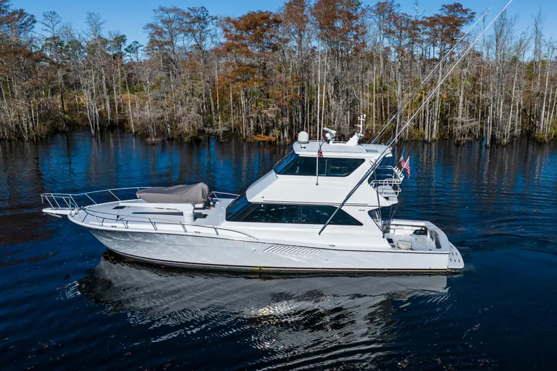 The Image of 1999 Viking 58 Convertible yacht cruising on a serene lake with forested shoreline. - 0