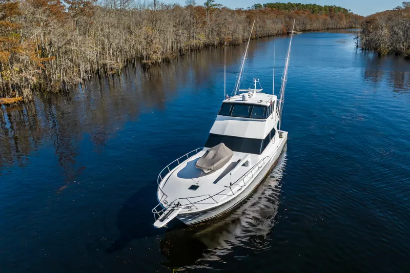Slide: The Image of 1999 Viking 58 Convertible yacht cruising on a serene river surrounded by trees. - 7