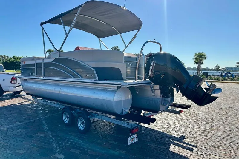Slide: The Image of 2023 Harris Cruiser 230 pontoon boat on trailer, parked outdoors under clear sky. - 3