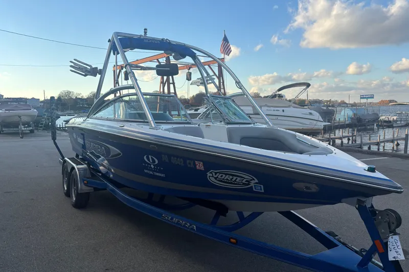 Slide: The Image of 2005 Supra Launch 22 SSV boat on trailer, dockside with clear sky and water background. - 6
