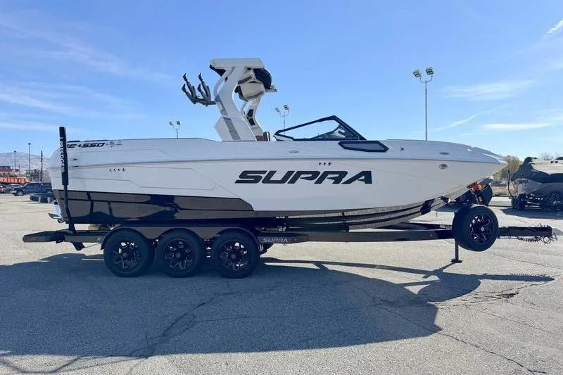 Slide: The Image of 2026 Supra SE boat on trailer, sleek design, parked outdoors under clear sky. - 1