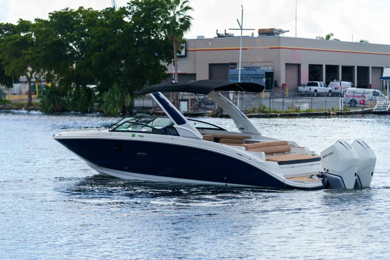 Slide: The Image of Sea Ray boat with dual Mercury engines cruising on a calm waterway near industrial buildings. - 2