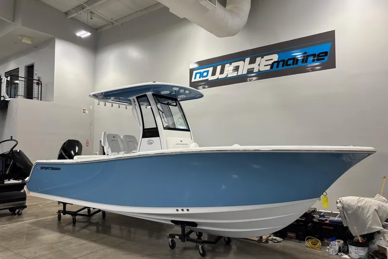 Slide: The Image of 2025 Sportsman Open 232 Center Console boat in showroom, blue hull, under "No Wake Marine" sign. - 2