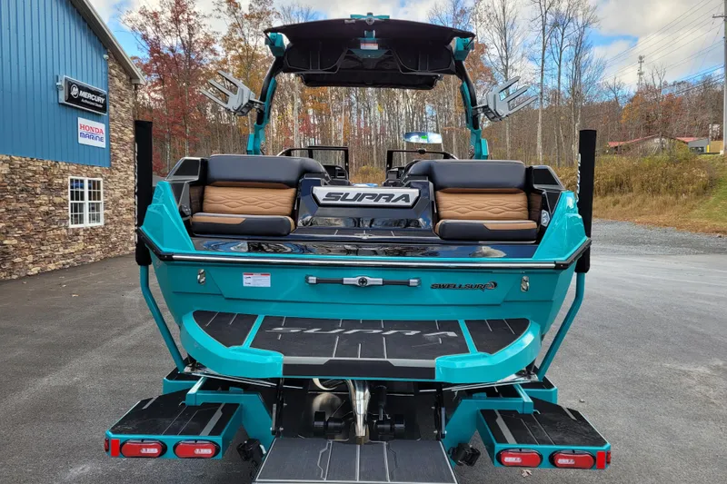 Slide: The Image of 2026 Supra SL boat with teal exterior, parked near a building, showcasing rear seating and design. - 6