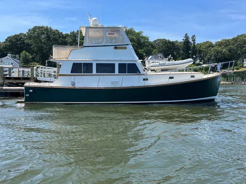 Slide: The Image of 1991 MDI Sedan Flybridge boat docked on calm water, surrounded by trees and houses. - 28