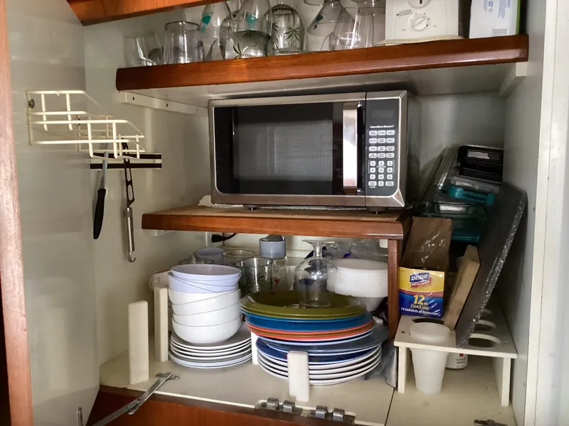Slide: The Image of Kitchen cabinet with microwave, stacked dishes, glasses, and utensils. MDI Sedan Flybridge 1991 model. - 7
