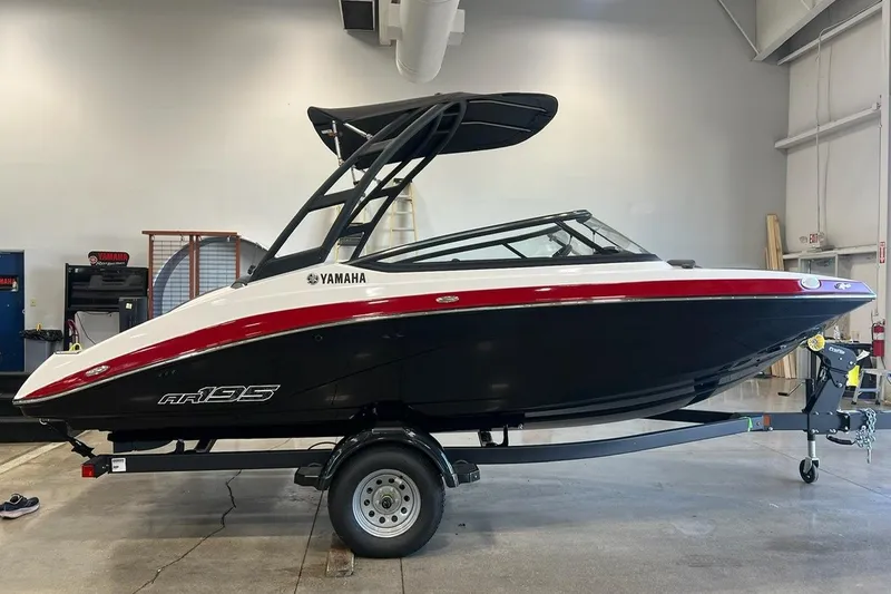 The Image of 2025 Yamaha AR195 boat in showroom, black and red design, on trailer. - 0