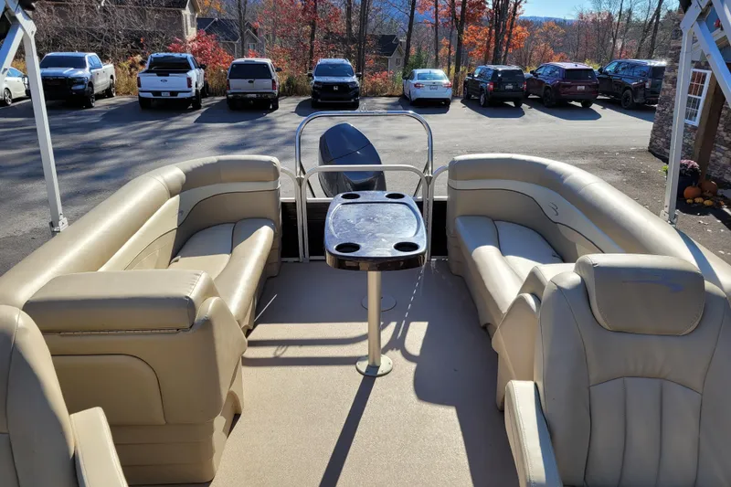 Slide: The Image of 2013 Bennington 24 SSRX pontoon boat interior with beige seating and table, parked outdoors. - 11