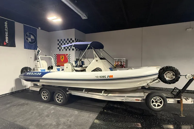Slide: The Image of 2021 Sealegs 7.5M RIB on trailer in showroom with racing flags. - 0
