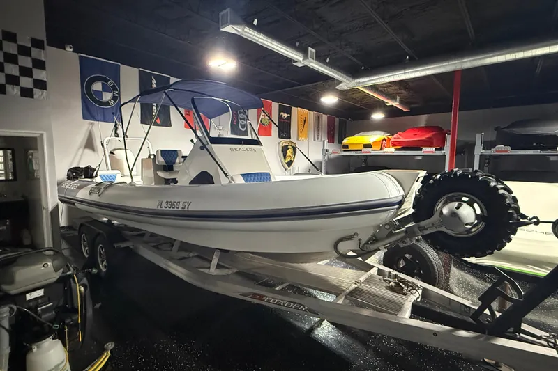 Slide: The Image of 2021 Sealegs 7.5M RIB boat on trailer in a garage with flags and cars. - 2