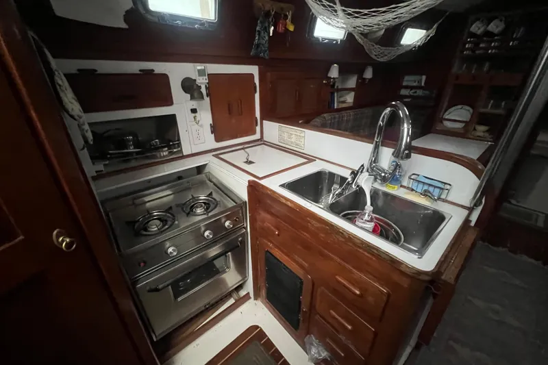 Slide: The Image of Cozy 1993 Com-Pac Sloop kitchen with stove, sink, and wooden cabinetry. - 29