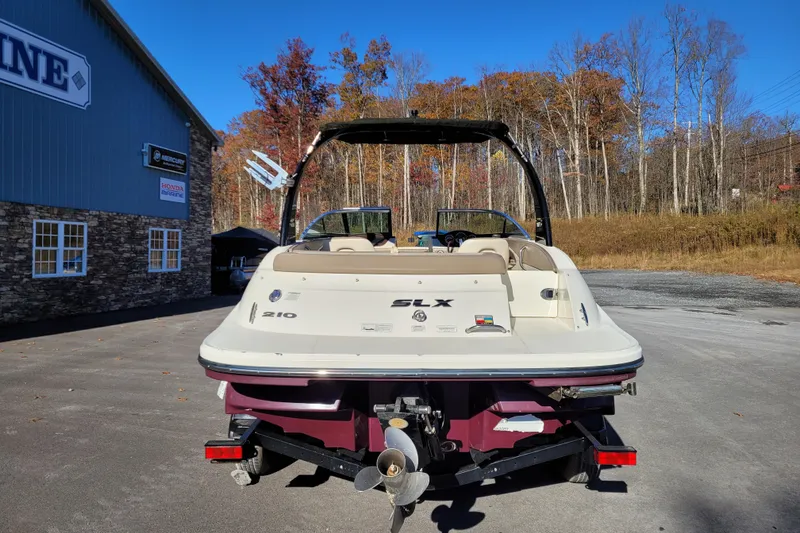 Slide: The Image of 2013 Sea Ray 210 SLX boat on trailer, parked near a marine building, autumn trees in background. - 7