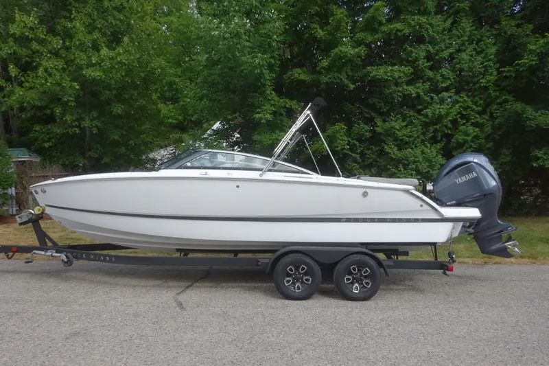 Slide: The Image of 2022 Four Winns H4 OB boat on trailer, parked on a road with lush green trees. - 4