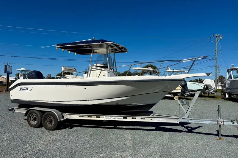 The Image of 2001 Boston Whaler 230 Outrage boat on trailer under clear blue sky. - 0