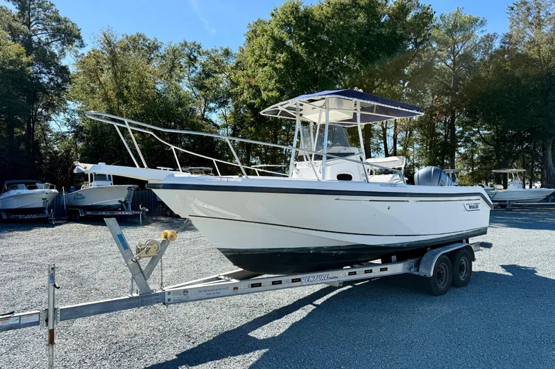 Slide: The Image of 2001 Boston Whaler 230 Outrage boat on trailer, parked outdoors with trees in background. - 9