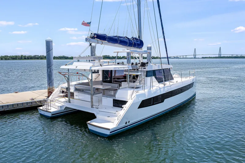 Slide: The Image of 2023 Leopard 42 catamaran docked in serene waters with a bridge in the background. - 2