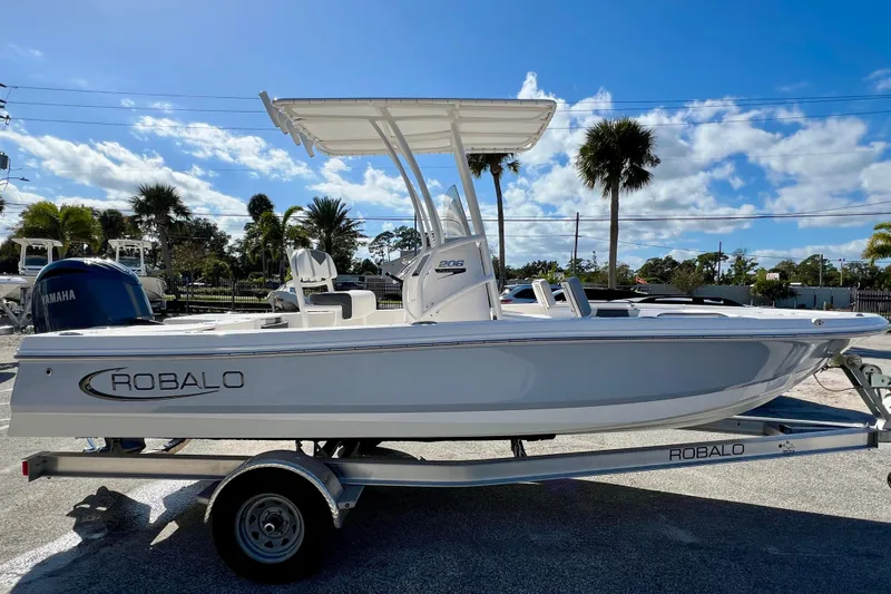 Slide: The Image of 2024 Robalo 206 Cayman boat on trailer, sunny day, palm trees in background. - 4