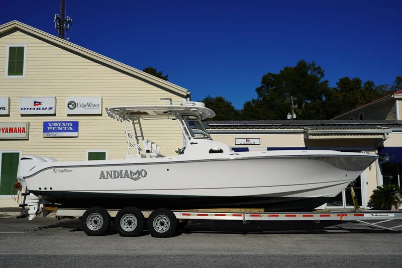 The Image of 2021 Edgewater 320CC boat on trailer, parked outside dealership with various brand signs. - 0