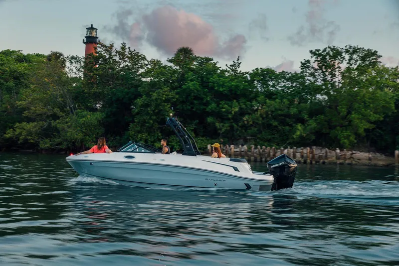 The Image of 2026 Bayliner VR6 Bowrider OB cruising on a scenic waterway near a lighthouse. - 0