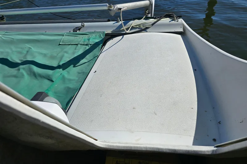 Slide: The Image of 1985 Sea Wind 24 sailboat deck with green cover, docked on calm water. - 13