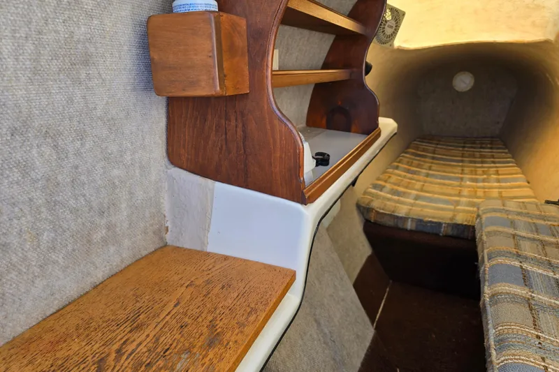 Slide: The Image of Interior of a 1985 Sea Wind 24 sailboat, featuring wooden shelves and plaid cushions. - 27