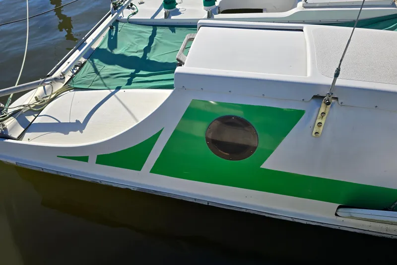 Slide: The Image of 1985 Sea Wind 24 sailboat with green accents and porthole, docked on calm water. - 28