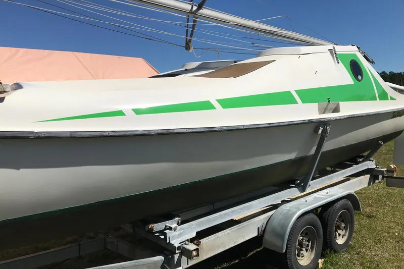 Slide: The Image of 1985 Sea Wind 24 sailboat on trailer, featuring green accents, under clear blue sky. - 7