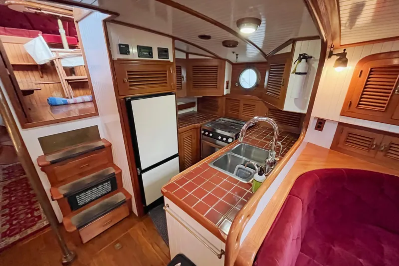 Slide: The Image of Cozy 1987 Liberty Gatsby yacht interior with wooden kitchen, red seating, and nautical decor. - 3