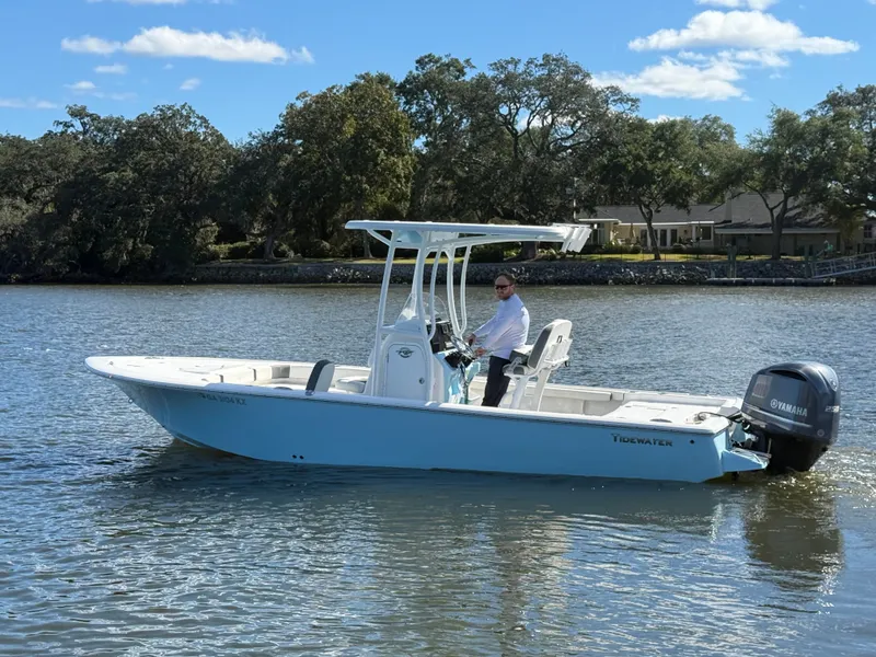 The Image of 2020 Tidewater 2300 Carolina Bay boat on water, with person steering, surrounded by trees. - 0