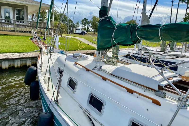 Slide: The Image of 1986 Bayfield 32 sailboat docked by a grassy shore, featuring green sail cover. - 16