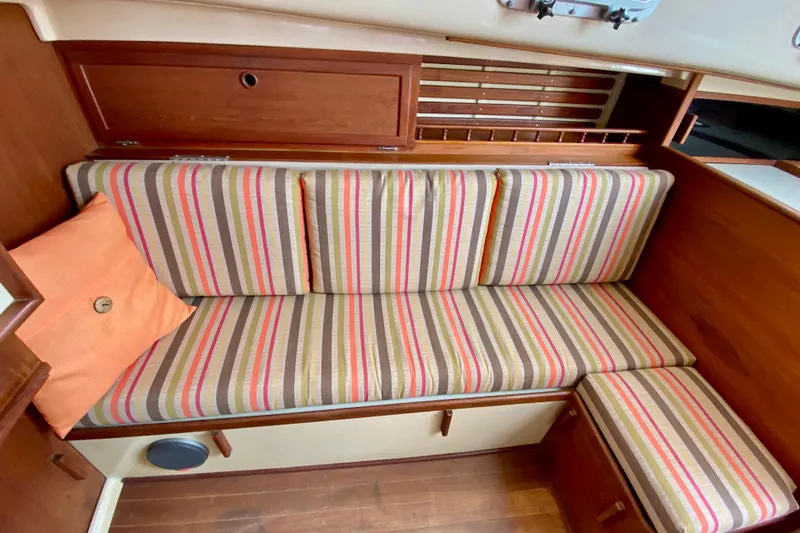 Slide: The Image of Striped seating area inside a 1986 Bayfield 32 sailboat, featuring wood accents and an orange pillow. - 42