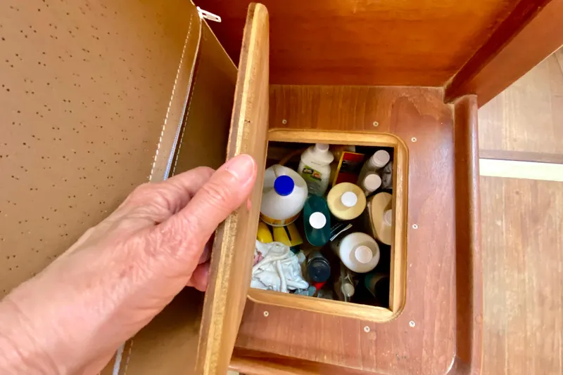 Slide: The Image of Hand opening storage compartment on 1986 Bayfield 32 boat, revealing cleaning supplies. - 48
