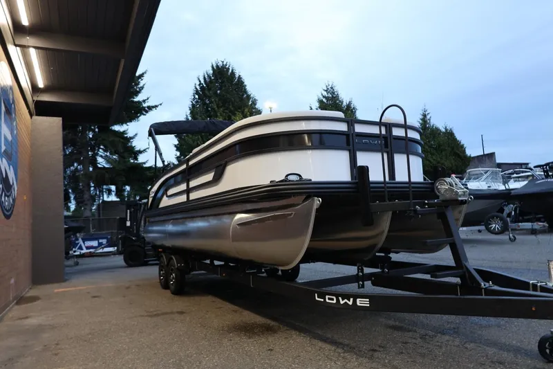 Slide: The Image of 2026 Lowe SS 230 CL pontoon boat on trailer, parked outdoors near a building. - 10