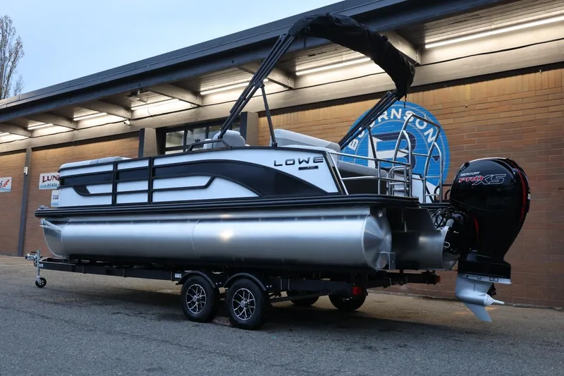 Slide: The Image of 2026 Lowe SS 230 CL pontoon boat on trailer, parked outside a building. - 4
