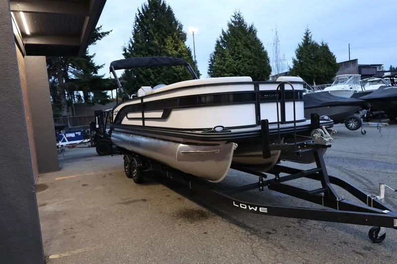 Slide: The Image of 2026 Lowe SS 230 CL pontoon boat on trailer, parked outdoors near trees. - 9