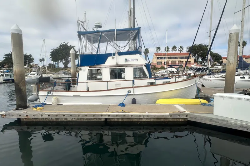 The Image of 1976 Grand Banks Sedan docked at marina, surrounded by sailboats and calm water. - 0